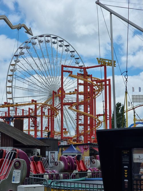 Free A ferris wheel and roller coaster at an amusement park under a blue sky day. Stock Photo