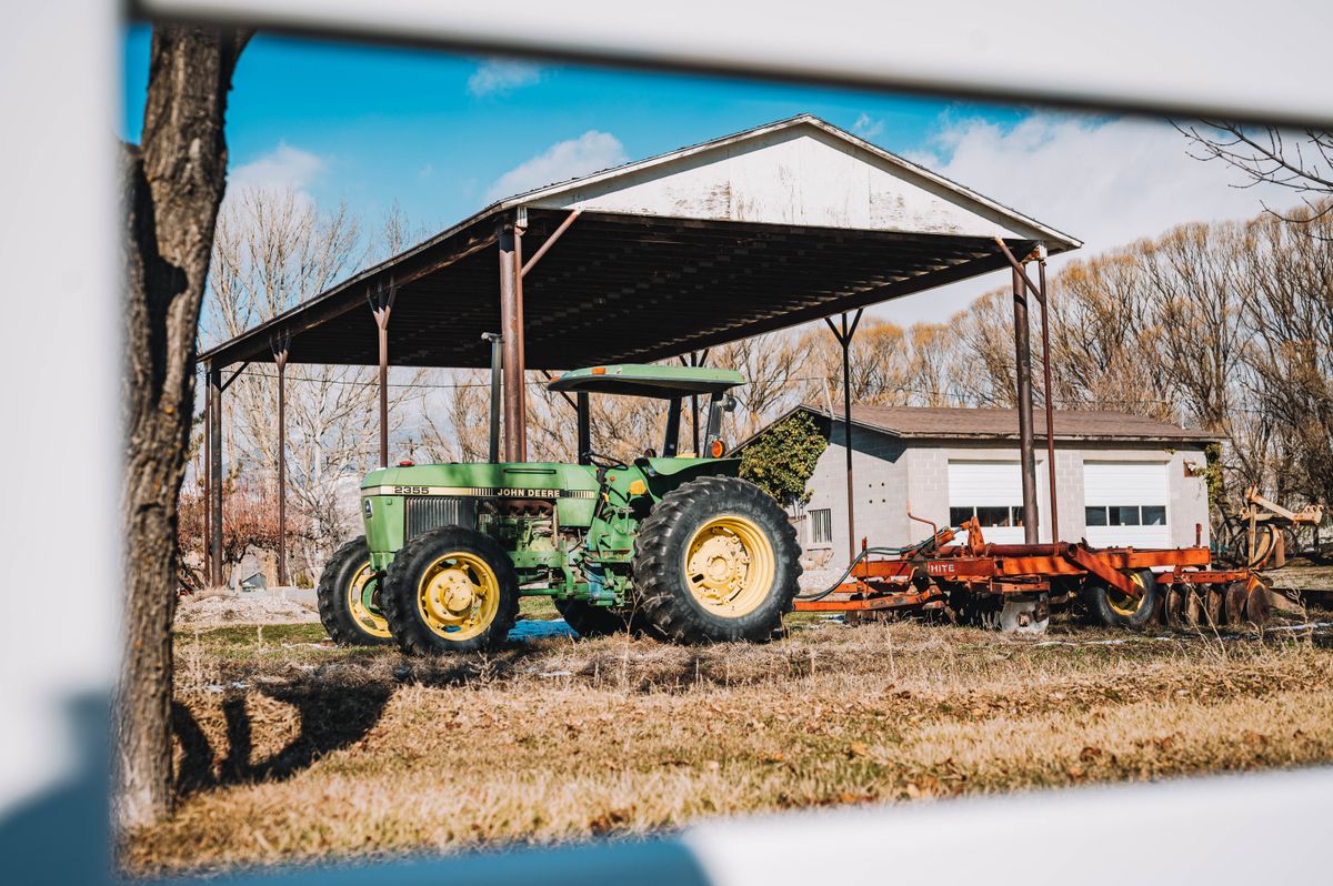 A green tractor parked under an open farm shed on a sunny day