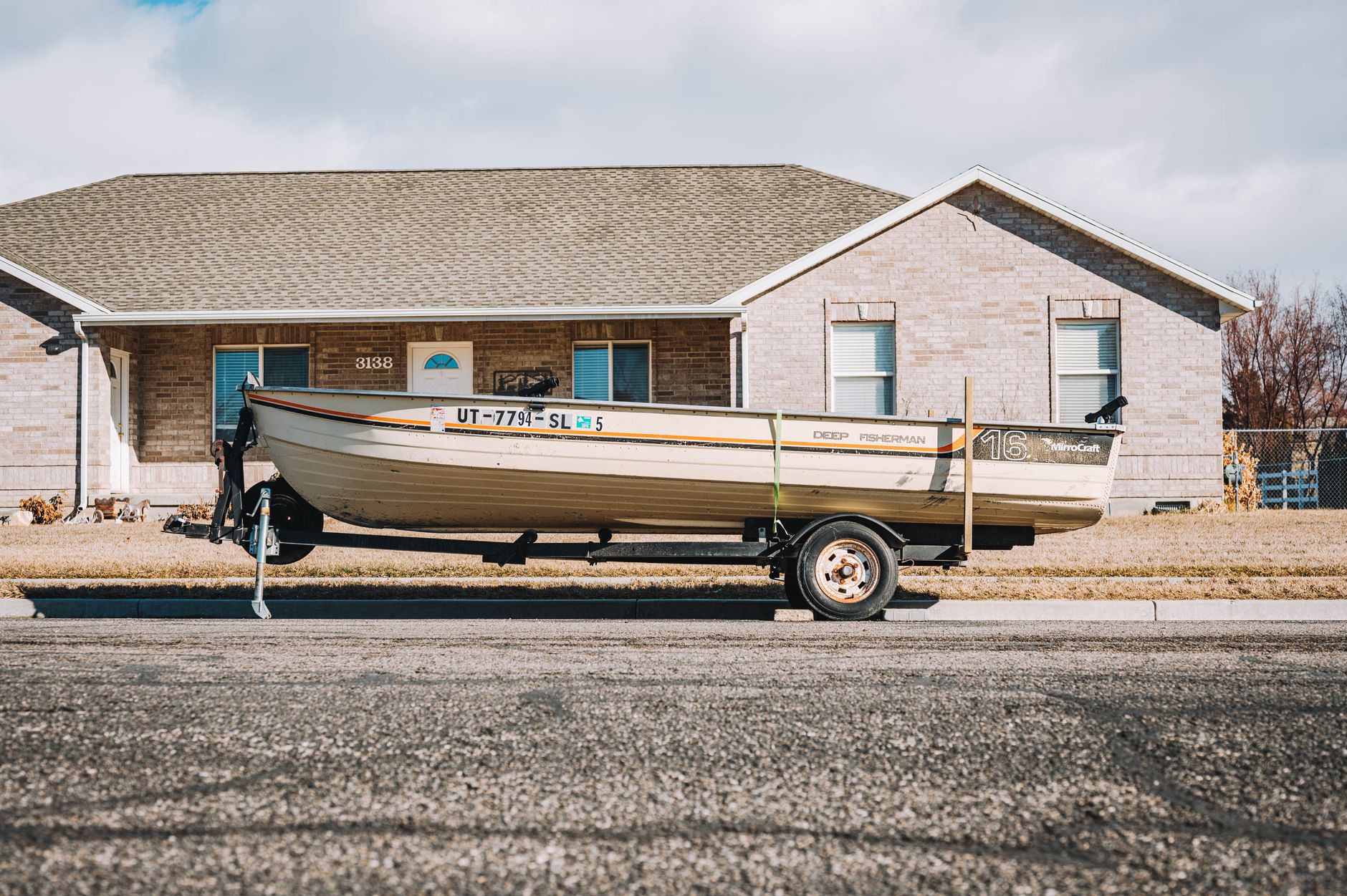 Small fishing boat on a trailer parked beside a suburban home, showing the sort of storage reality first-time tinnie owners need to consider.