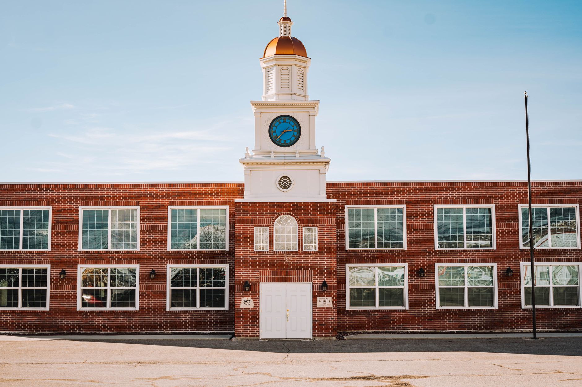 A red brick building with a clock tower and white accents stands under a clear blue sky, offering architectural charm.