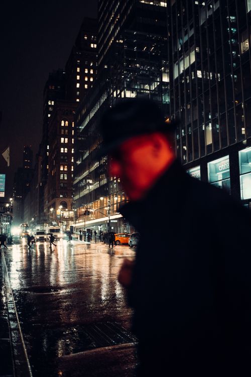 Free A man in a hat walks through a rainy, illuminated city street at night with blurred lights. Stock Photo