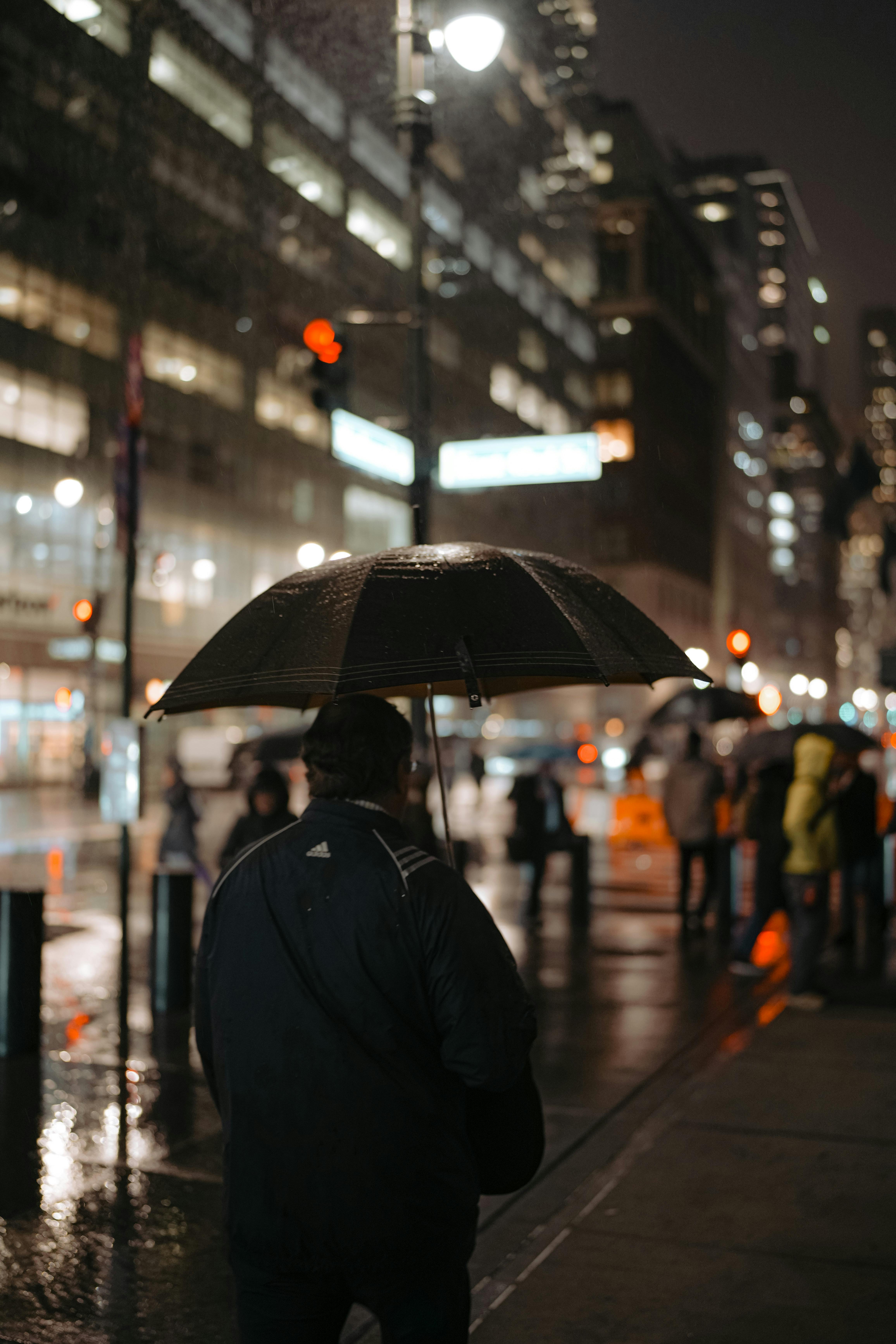 A city street scene on a rainy night with pedestrians and city lights reflecting on wet pavement.