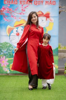 Mother and daughter wearing red dresses pose at a cultural festival outdoors.