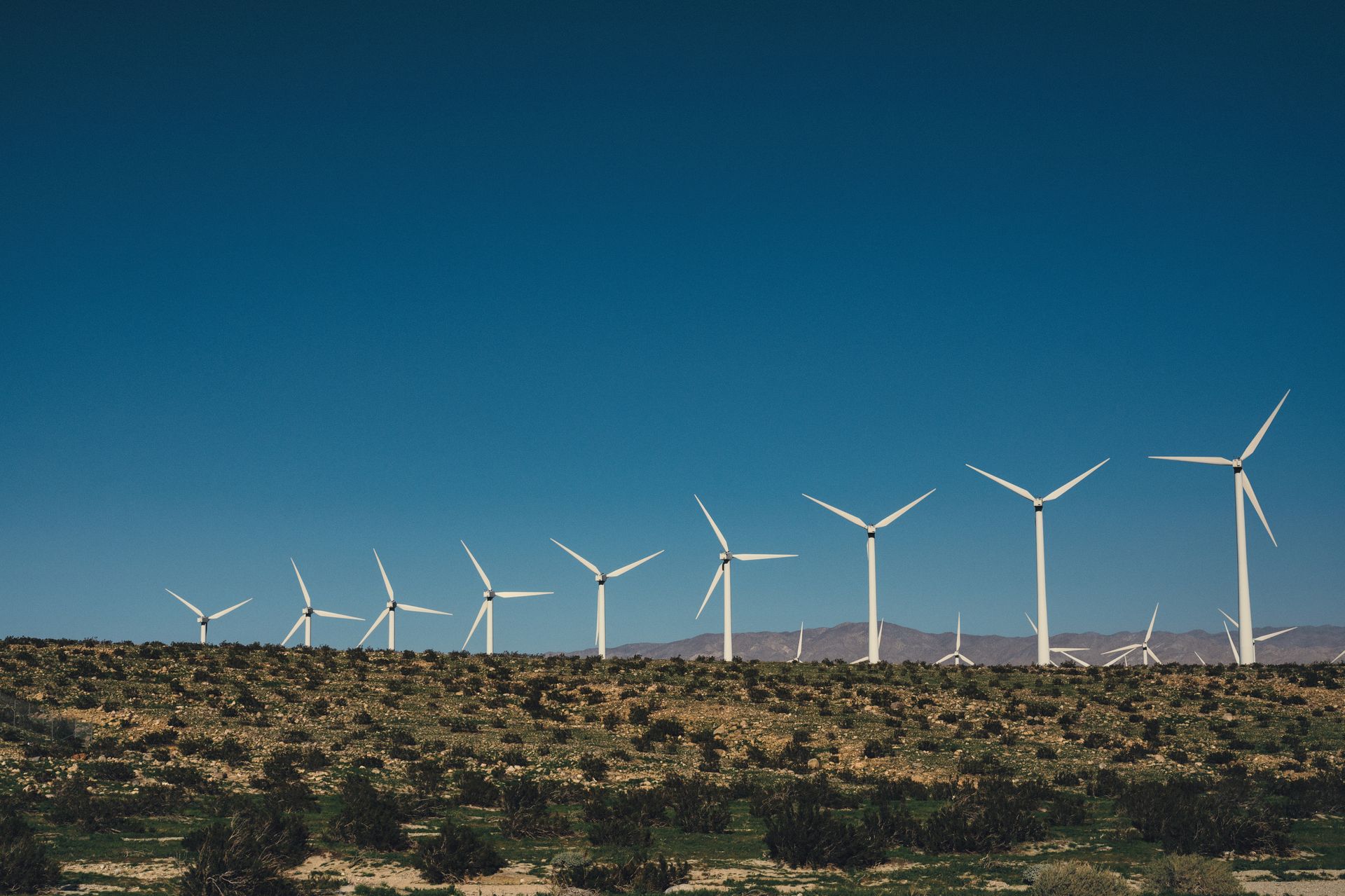 Row of wind turbines on a field, generating renewable energy under a clear blue sky.