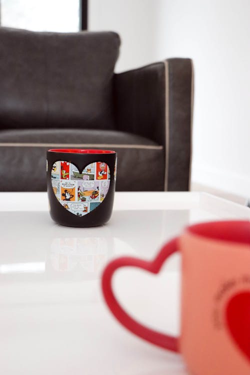 Two mugs with hearts on them sit on a table