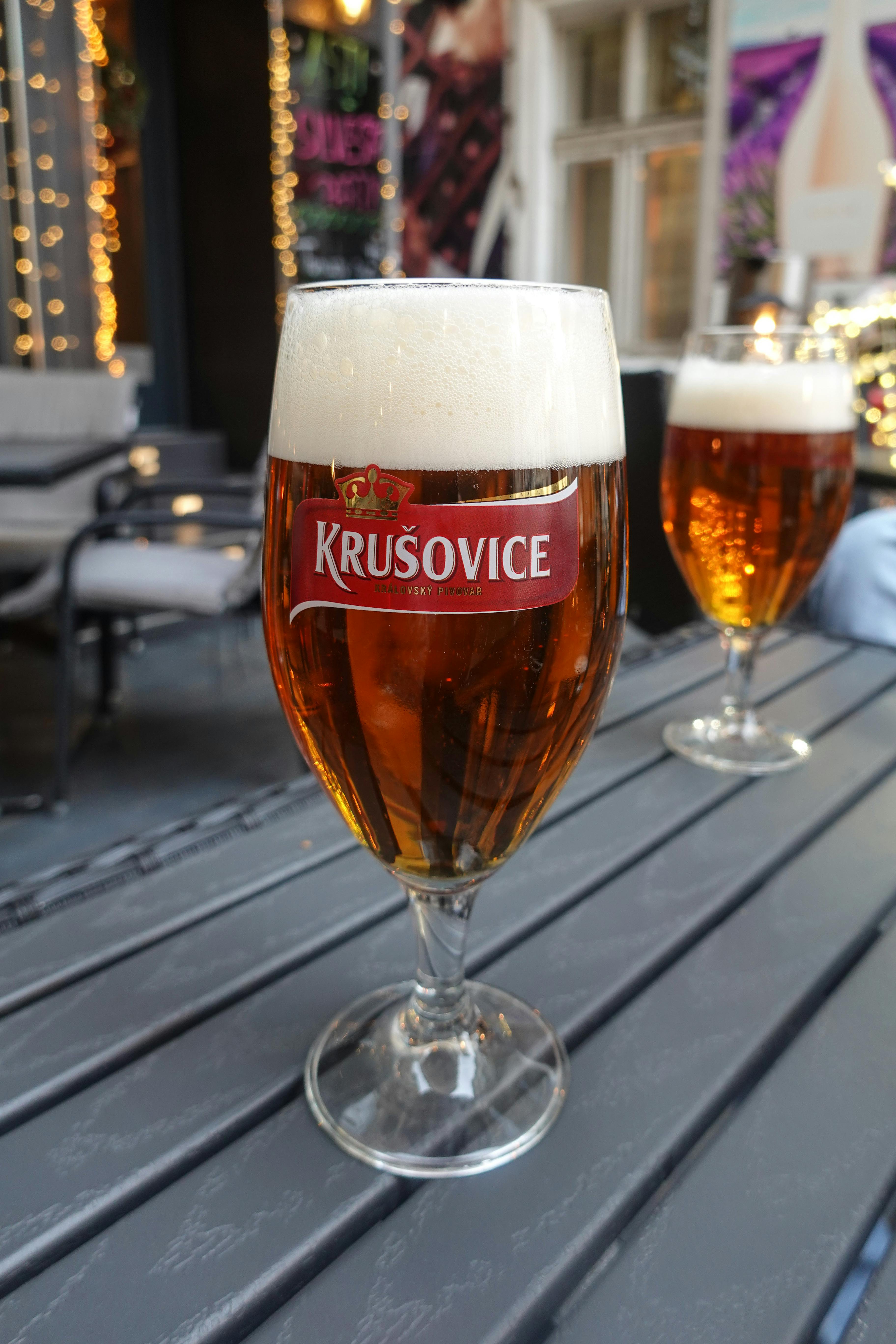 A close-up of Krusovice beer glasses on a table in a cozy outdoor setting, perfect for a casual drink.