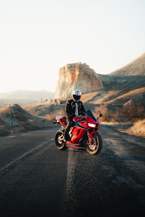 Free A motorcyclist rides down an open highway near a stunning rock formation, capturing the essence of adventure and travel. Stock Photo
