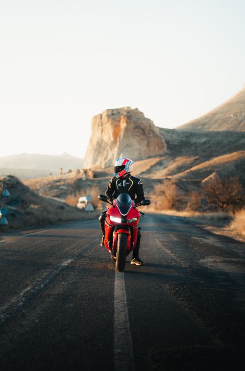 Free Motorcyclist rides on a quiet road with stunning desert mountain scenery, highlighting travel adventure. Stock Photo