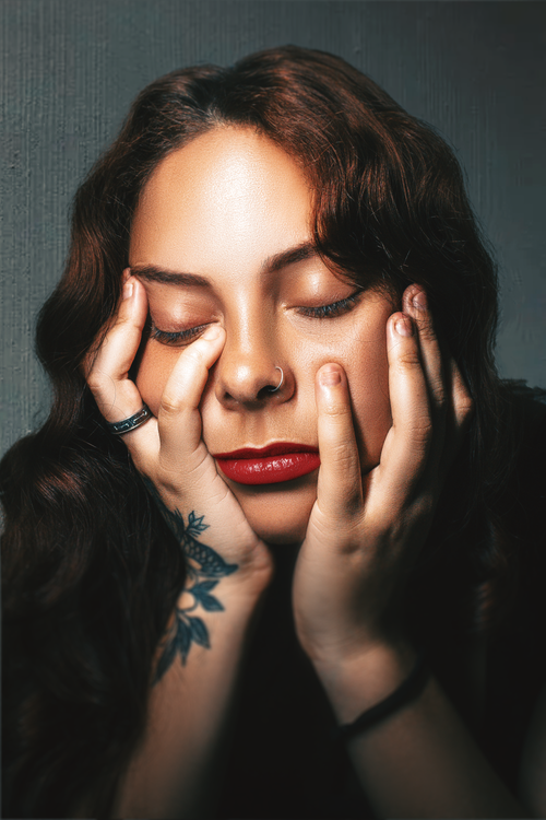 Free Serene portrait of a young woman with tattoos and red lips, eyes closed, in a studio setting. Stock Photo
