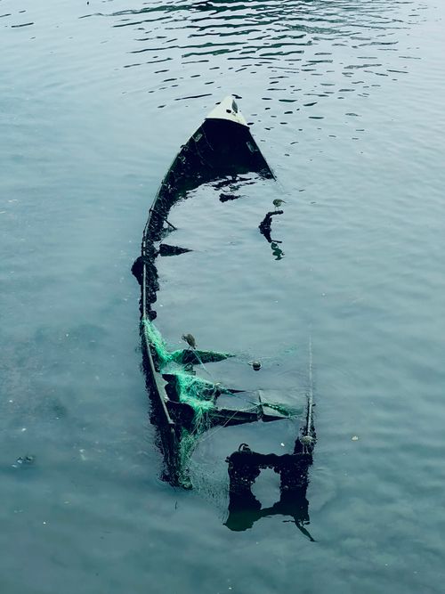 Free Eerie sunken boat partially submerged in calm blue waters, viewed from above. Stock Photo