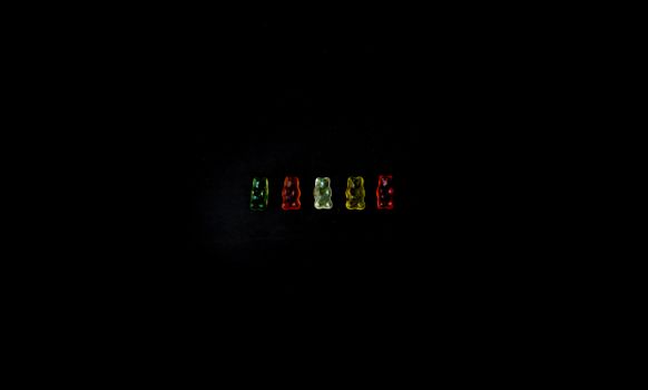 A studio shot of colorful gummy bears aligned on a black background.