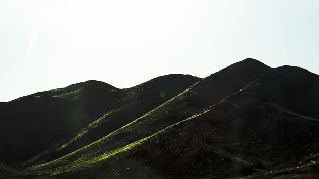 A scenic view of sunlit green hills under a bright clear sky, featuring subtle lens flare effects.