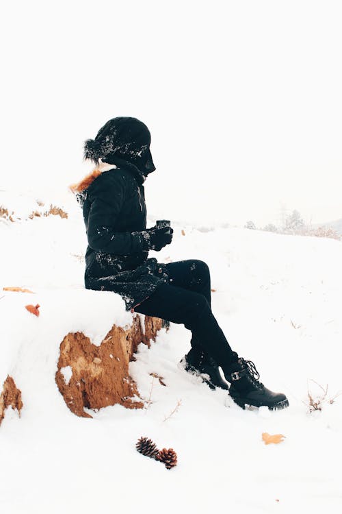 Woman in Warm Clothing Sitting Outdoors in Snow 