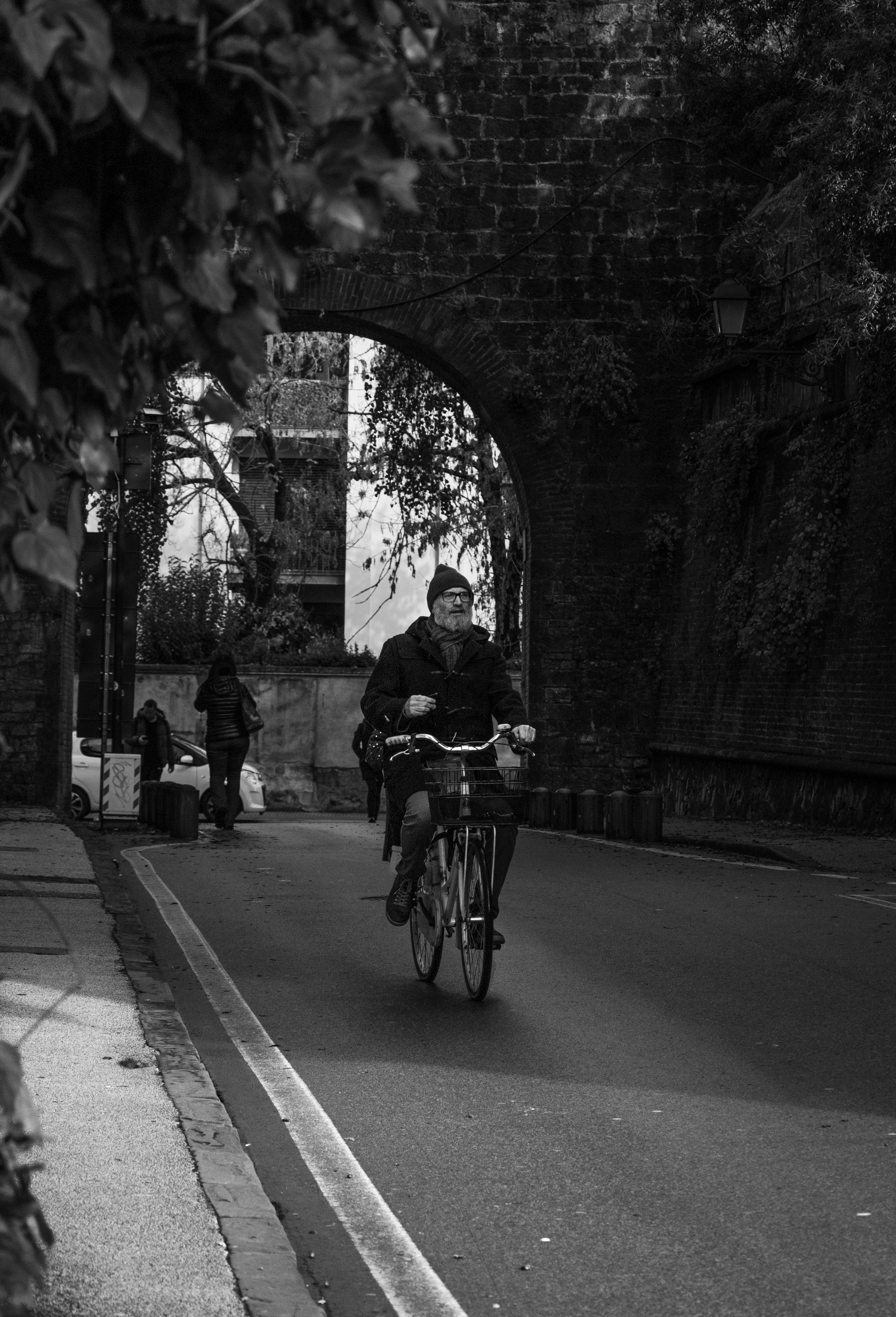 A man rides a bicycle through the historic streets of Pisa, Italy. Black and white captures the urban vibe.