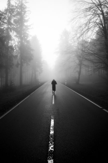 Atmospheric black and white photo of a foggy road in Feldberg, Germany, with a solitary figure.