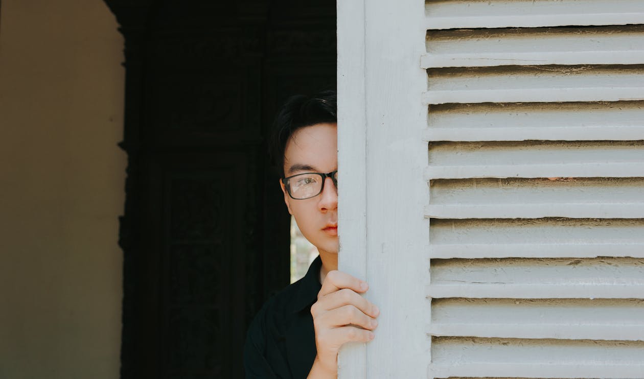 Free Man Sneaking Behind White Louvered Wall Stock Photo