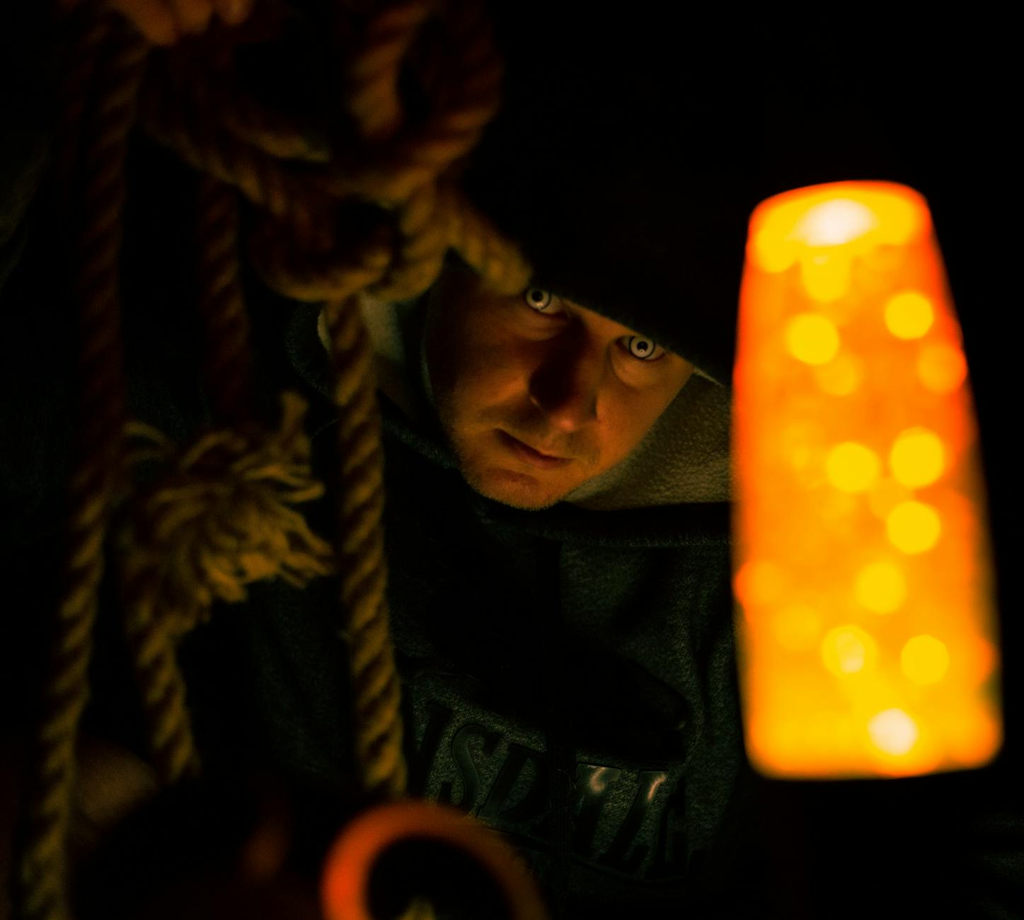 A man illuminated by a lamp holds ropes, creating a moody and suspenseful atmosphere.