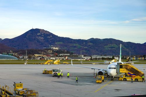 Free Commercial airliner on Salzburg airport tarmac with scenic Alps in background on a clear day. Stock Photo