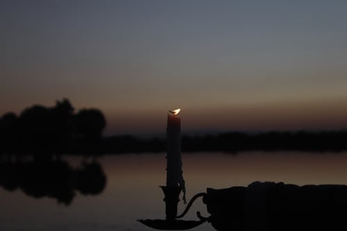 Silhouetted Hand Holding a Candle on the Background of a Lake at Sunset 