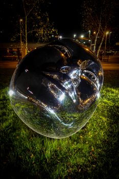 Metallic head sculpture illuminated at night in a modern park setting. Captivating and artistic.