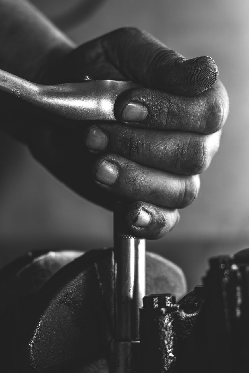 A detailed black and white image of human hands gripping a metal tool, conveying industrial work.