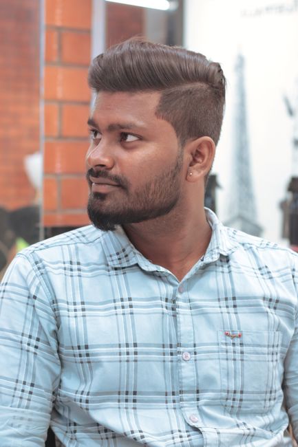 Casual indoor portrait of a young man with a beard and moustache wearing a checked shirt and looking aside.