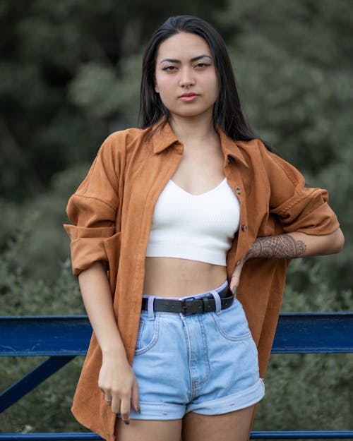 Free Young Woman in a White Top, Shirt and Denim Shorts Standing Outside  Stock Photo