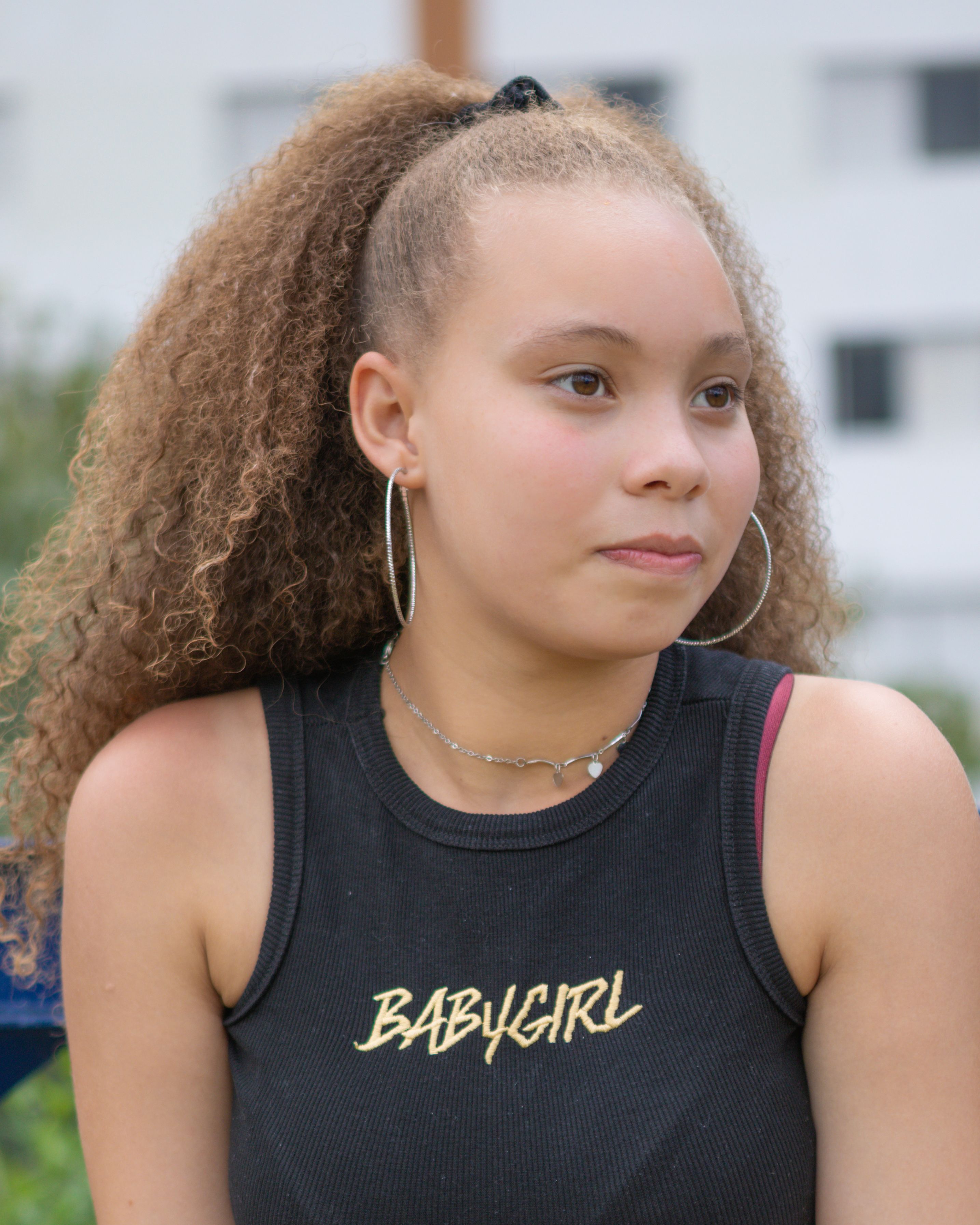 A thoughtful teenager with curly hair and hoop earrings, posing in an outdoor setting.