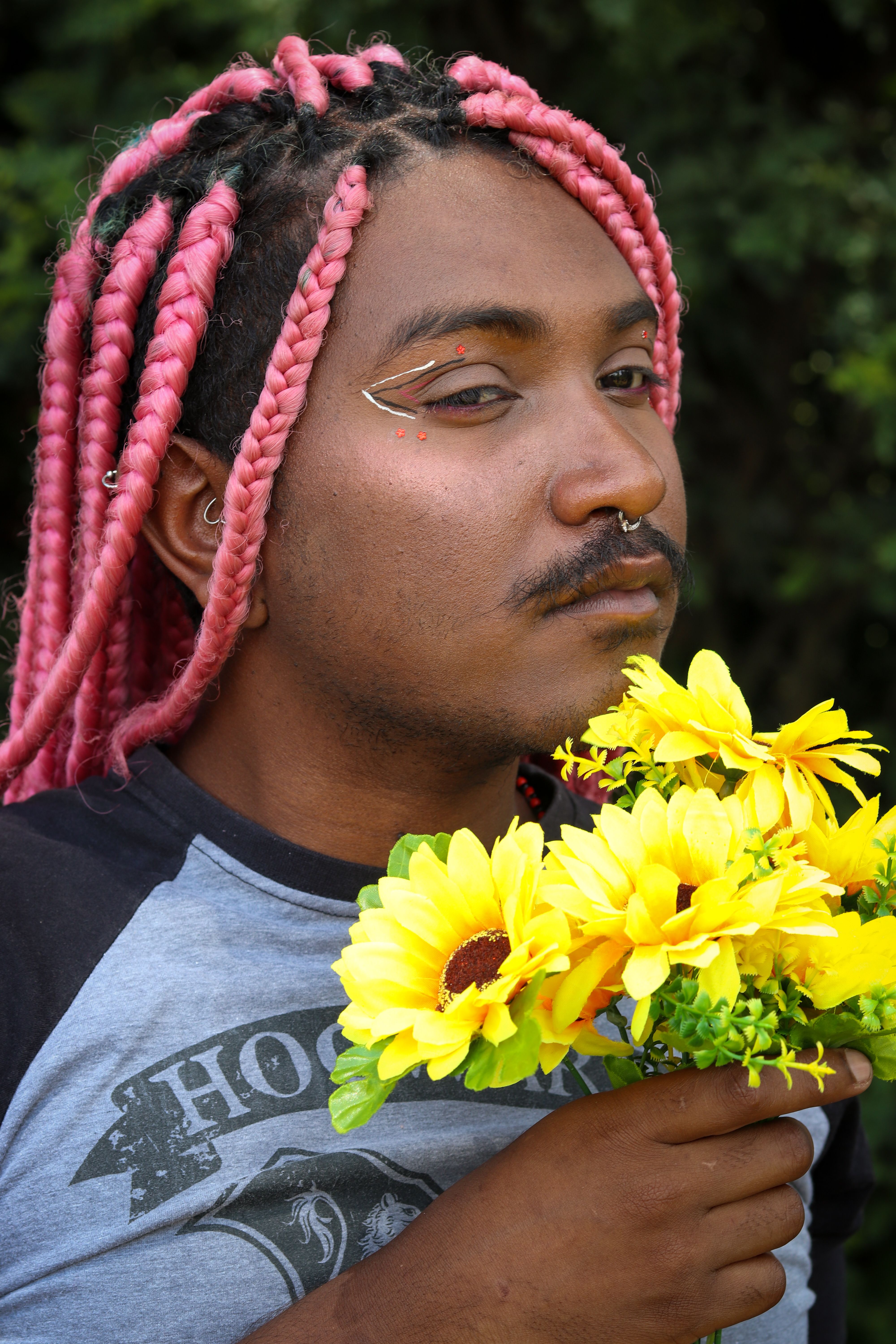 A striking portrait of a man with pink braided hair holding sunflowers.