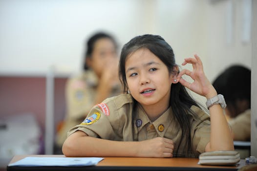 Teenage girl in school uniform sitting at desk in a classroom setting, appearing relaxed and attentive.
