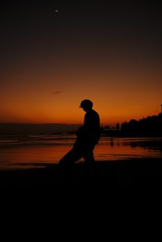 A silhouette of a person walking on a beach during a vibrant sunset with trees in the background.