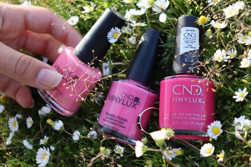 Vibrant pink nail polish bottles in a fresh outdoor setting with daisies, showcasing beauty and nature.