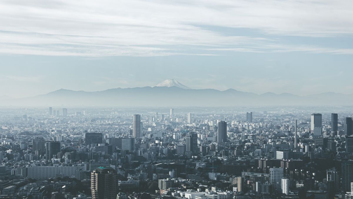 도쿄 — Panoramic view of Tokyo cityscape with Mount Fuji looming in the background, under cloudy skies.