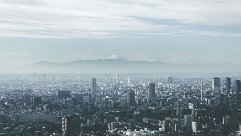 Panoramic view of Tokyo cityscape with Mount Fuji looming in the background, under cloudy skies.
