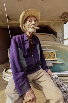 Senior man in a hat smoking a cigar beside a classic vintage car outdoors.