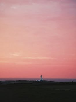 Majestic lighthouse under a vibrant sunset sky along a serene coastline.