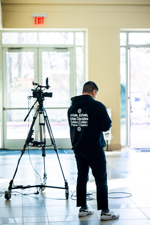 Man Standing near Camera on Tripod in Room