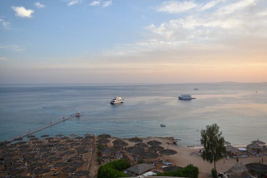 Stunning aerial view of Sharm El Sheikh's beach and sea during sunset with boats and parasols.