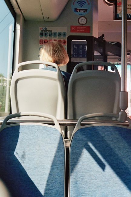 View from a bus, showing empty seats and a lone passenger in daylight.