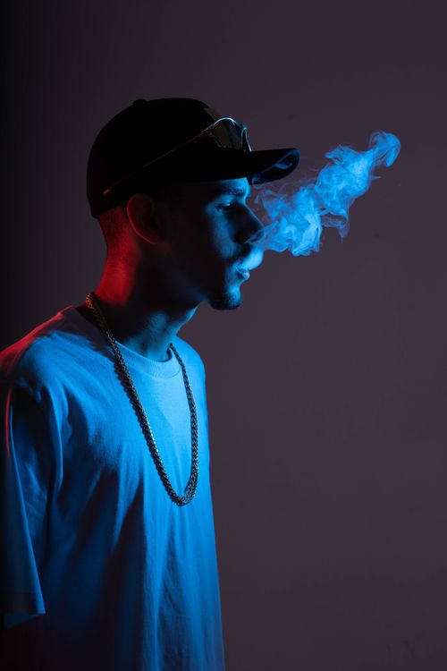 Free Side profile of a man in cap exhaling smoke with dramatic lighting in studio setting. Stock Photo