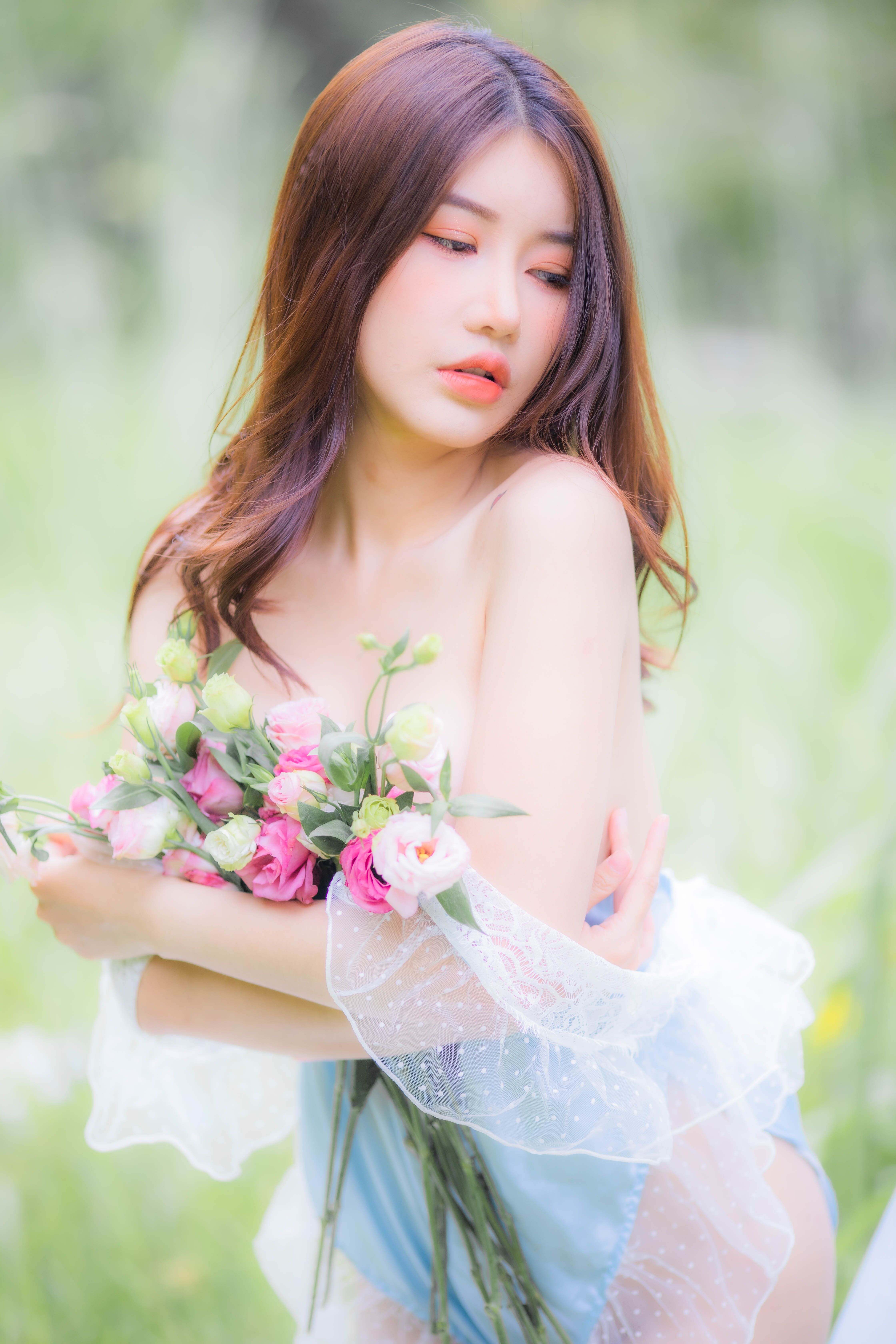 Asian woman posing gracefully with a bouquet of flowers in a serene outdoor setting.