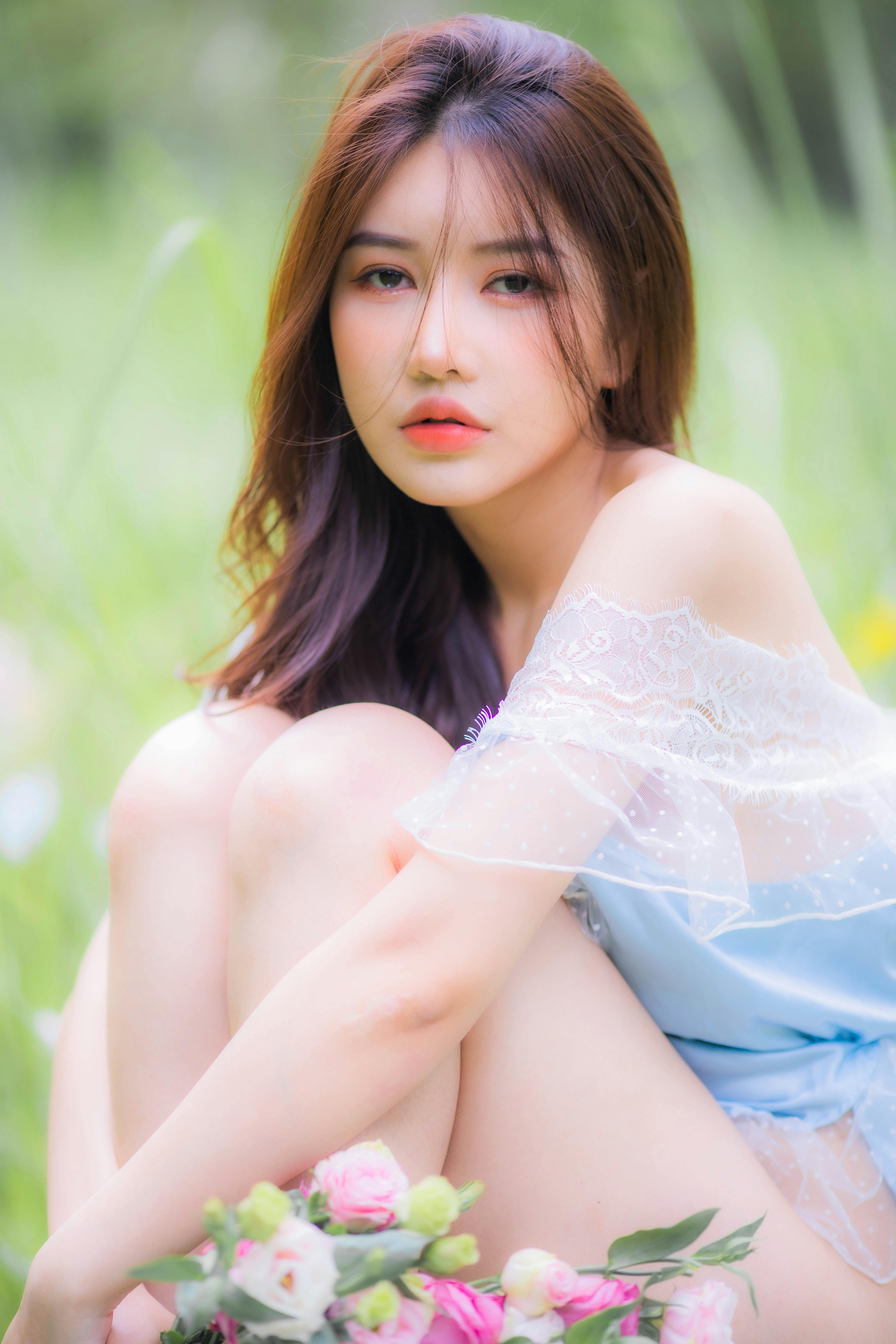 A serene portrait of a woman sitting outdoors surrounded by flowers, exuding tranquility.