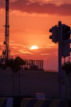Vibrant sunset over industrial landscape with traffic lights and tower silhouette.