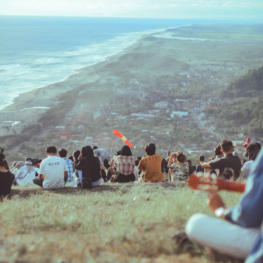 People sitting on a hillside above a festival site — photo by Djaja Suara on Pexels