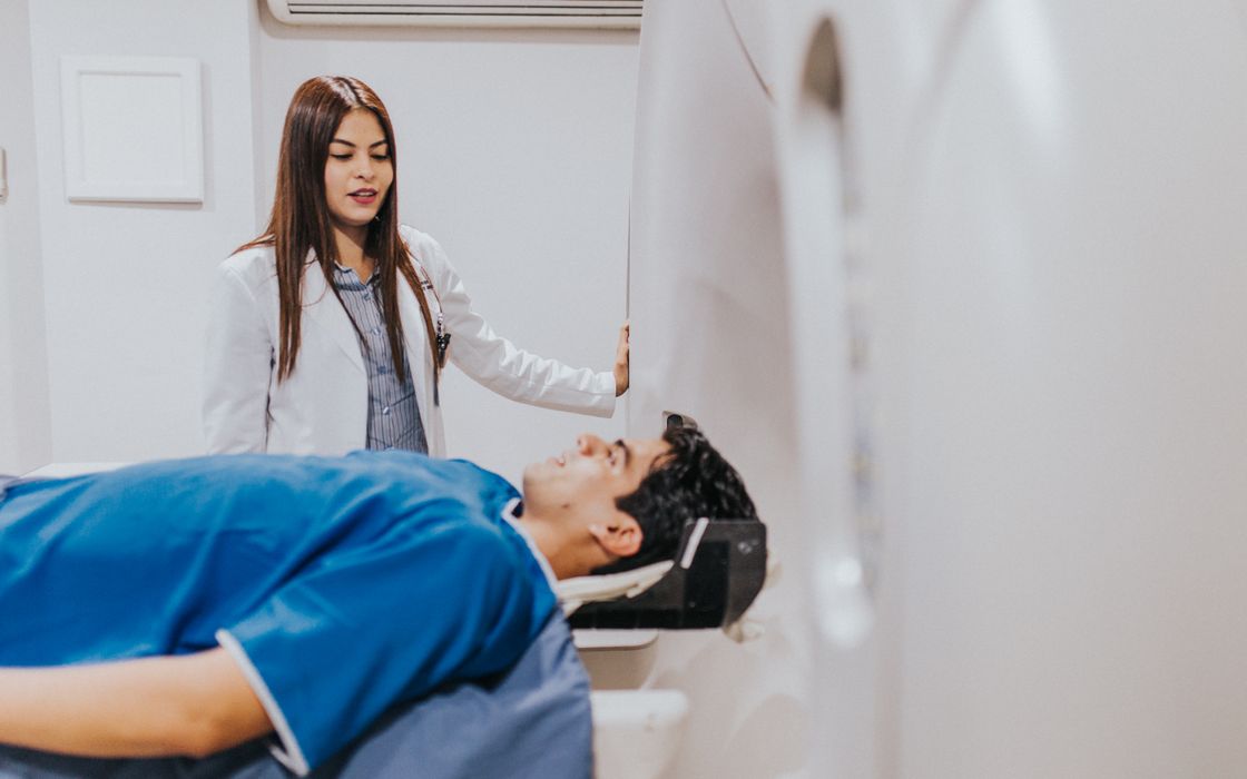 A doctor stands beside a patient lying on an MRI scanner table before a scan