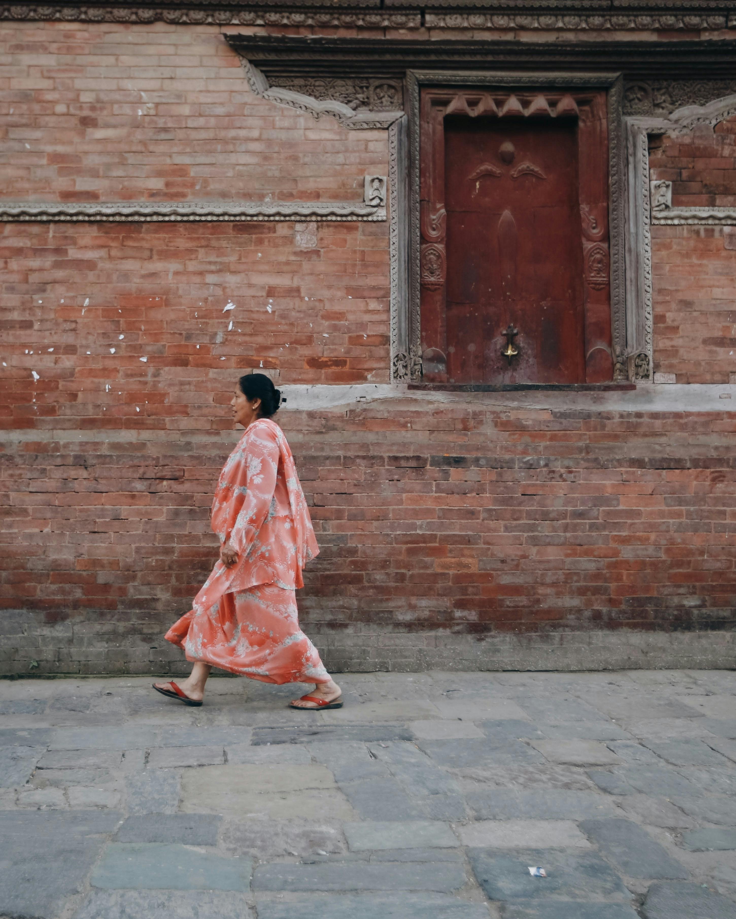 A woman in a floral kimono walks by a traditional brick wall with ornate doorway.