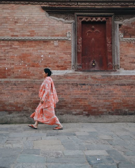 A woman in a floral kimono walks by a traditional brick wall with ornate doorway.