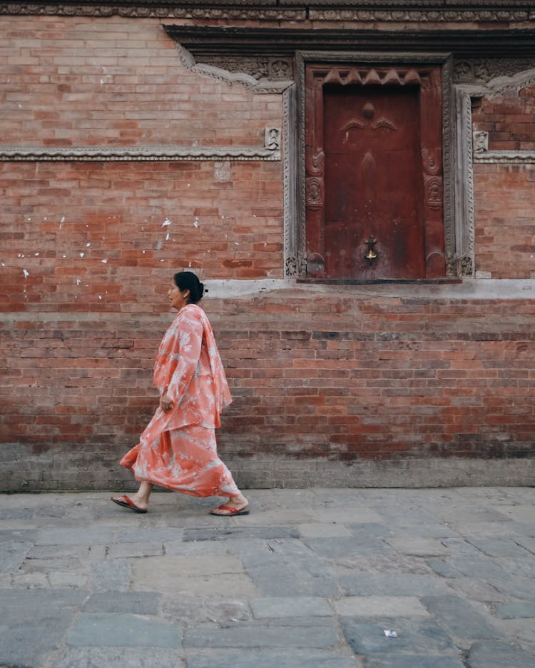 Woman In Traditional Clothes Walking Near Brick Wall