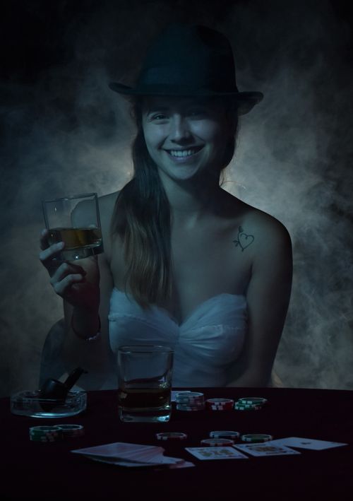 Free Smiling woman in a tube top, holding a drink, with poker chips and cards on the table, in a dimly lit room. Stock Photo