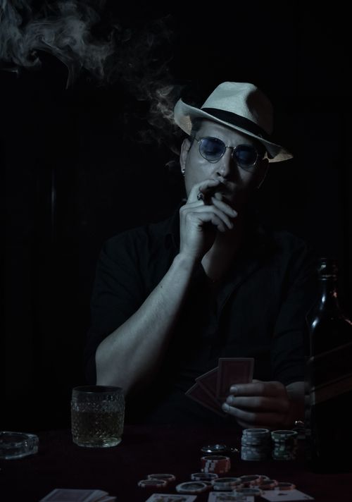 Free A mysterious poker player with a cigar and whiskey, exuding a noir atmosphere. Stock Photo